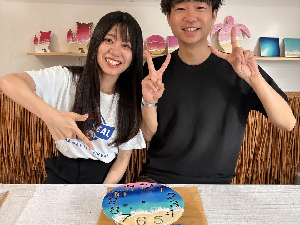 完成した時計の作品を前に、笑顔でピースをする2人の参加者