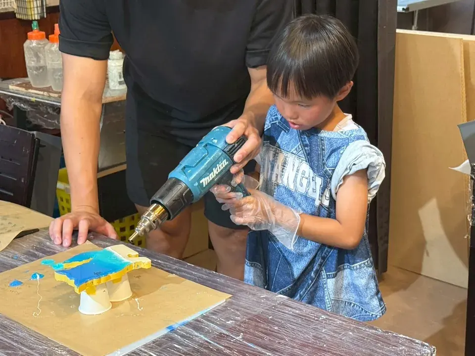 大人に支えてもらいながら、ヒートガンで作品に波模様をつくる男の子